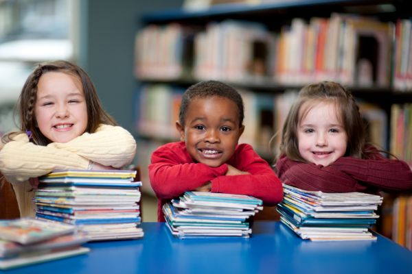 Drei Kinder sitzen in einer Bibliothek